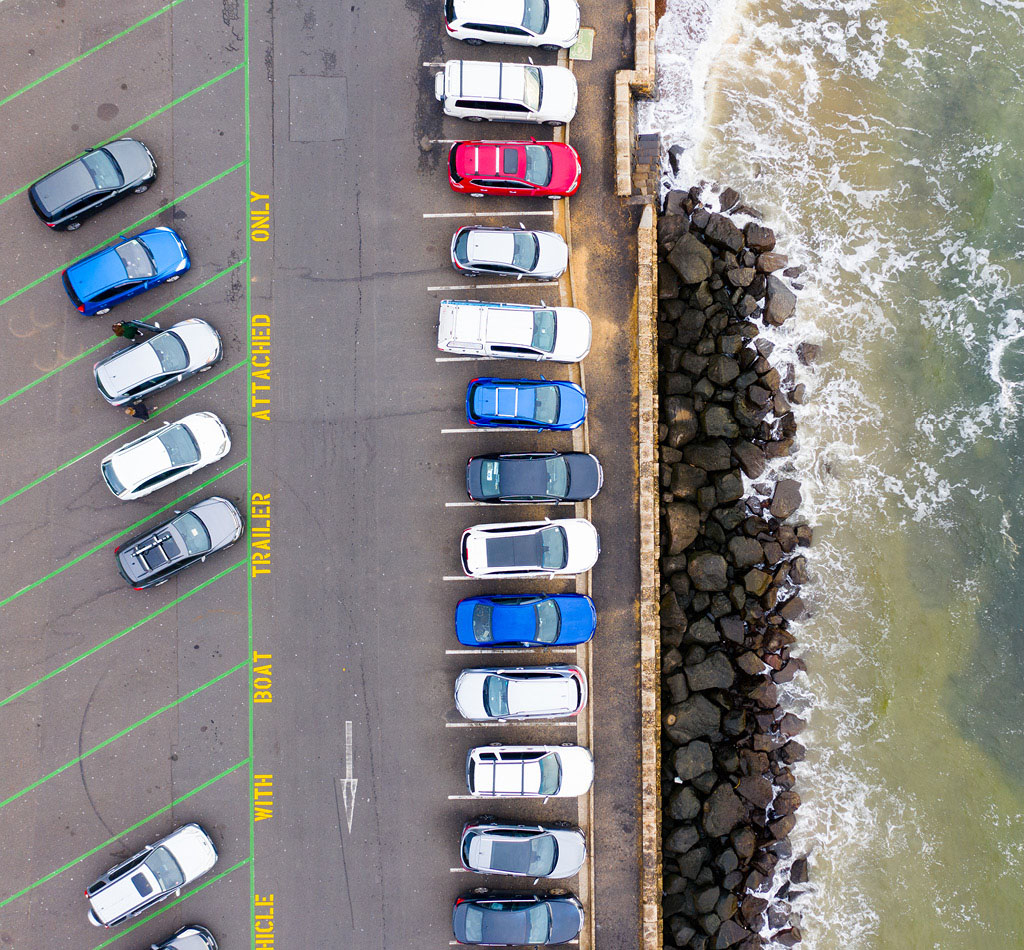 Aerial photograph of a coastal car parking lot as waves break nearby.
