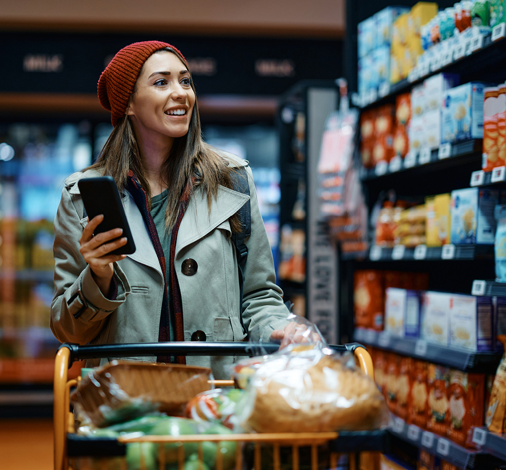 Smiling woman holding mobile phone shopping in grocery store.