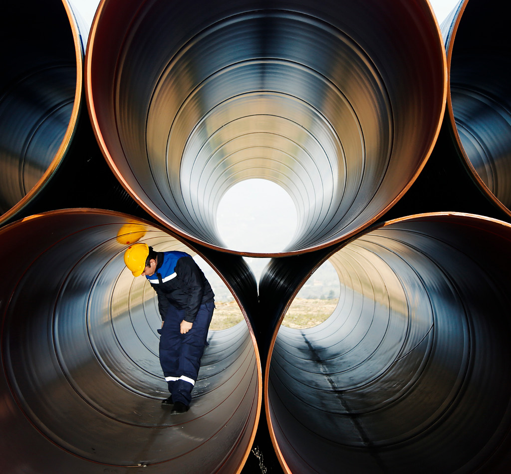 Engineer checking and walking through a stack of industrial pipes at a construction site.