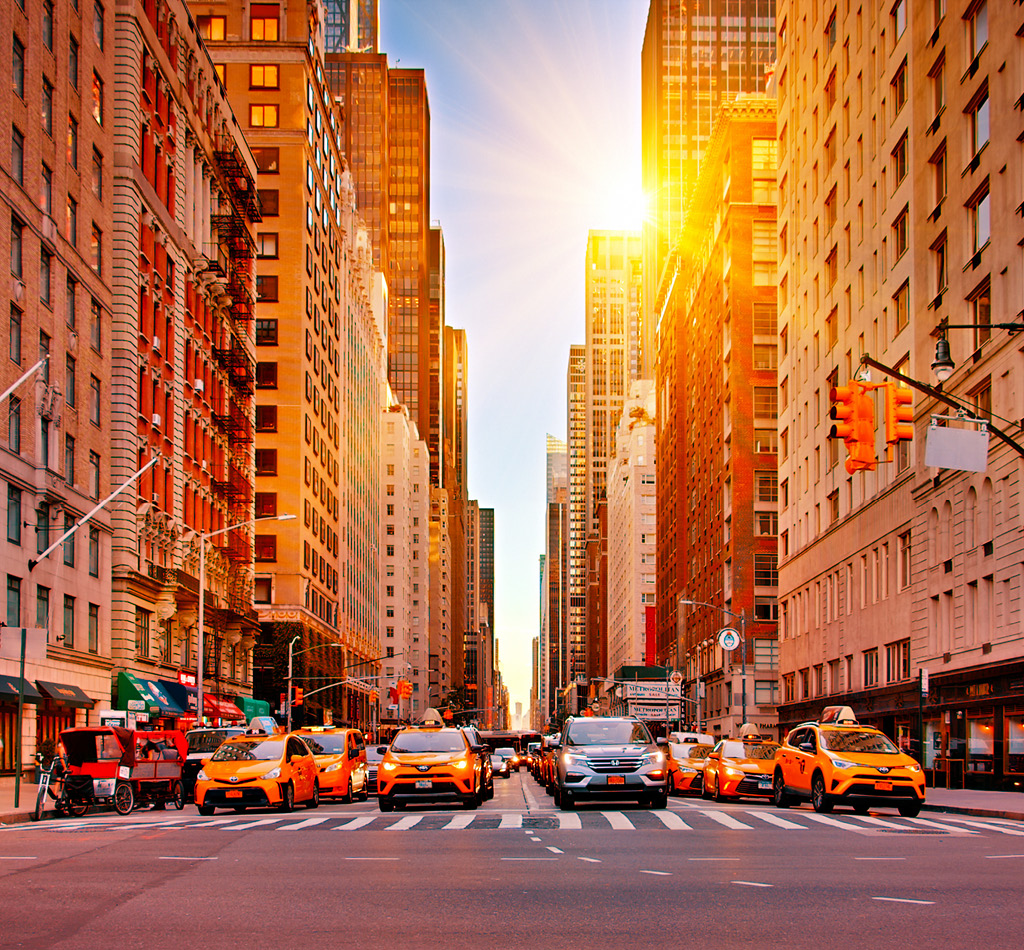 A busy intersection in New York City with bright sunlight in the background.